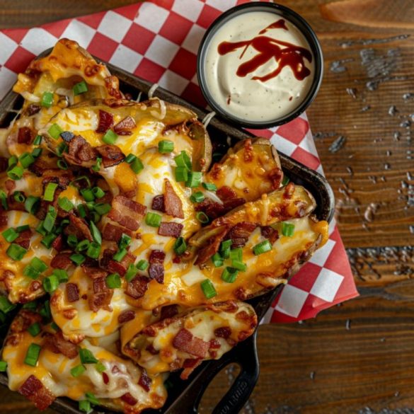 Friday’s Potato Skins A plate of TGI Friday's-style potato skins, generously topped with melted cheddar cheese, crispy bacon bits, a dollop of sour cream, and a sprinkle of fresh green onions.